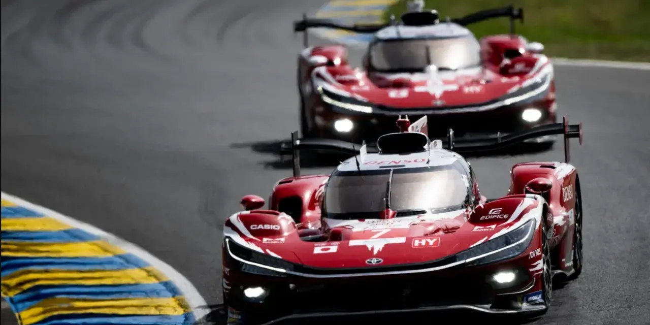 Dos coches de carreras rojos compiten en Le Mans, sus luces brillan en la pista.