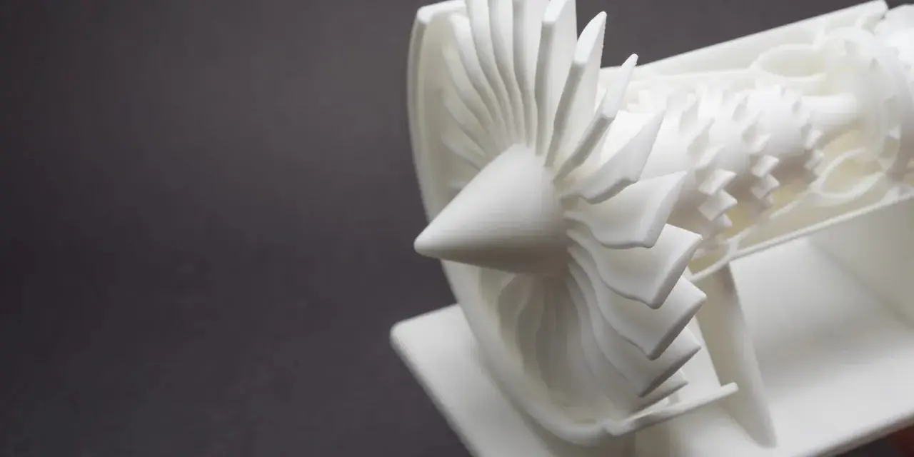 A detailed white model of a jet engine's turbine, showcasing intricate blades, likely created by a laser sintering machine.
