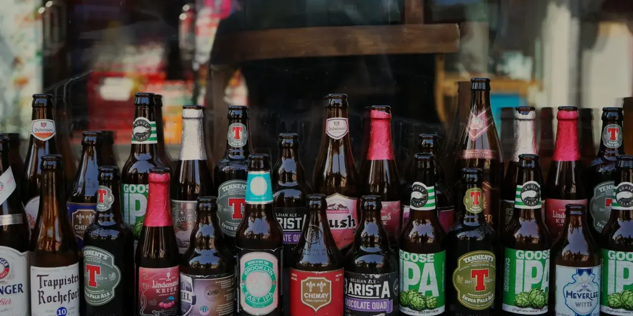 Rząd butelek z piwem kraftowym, w tym Trappistes Rochefort, Chimay, Goose Island i inne. Idealne na pytanie: jakie piwo kraftowe wybrać?