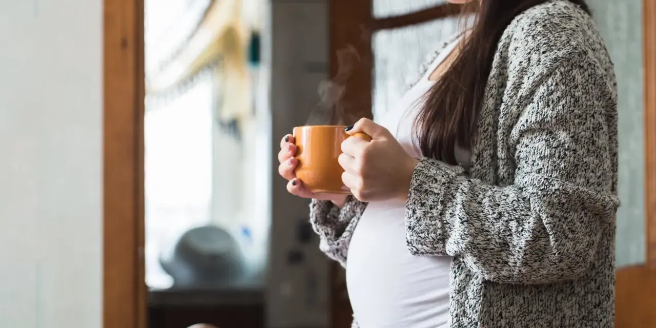 Ciepły napar z rooibos w dłoniach ciężarnej kobiety. Delikatny dym unosi się z kubka, tworząc chwilę spokoju.