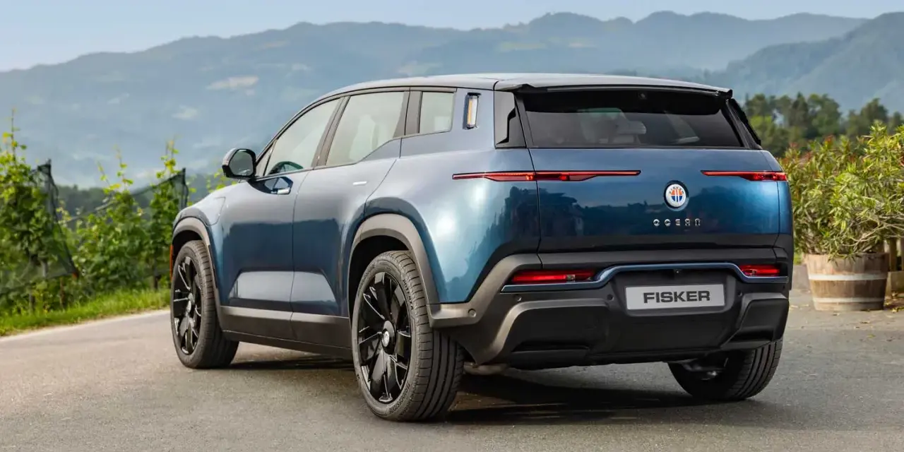 Tylna część niebieskiego elektrycznego SUV-a Fisker Ocean na tle gór i zieleni.