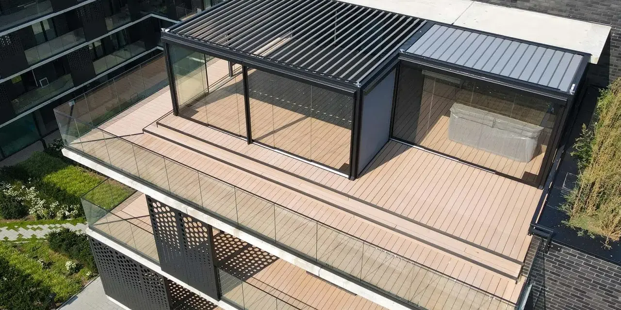 Nowoczesny taras na dachu z przeszklonym pawilonem i pergolą. Drewniana podłoga i szklane balustrady tworzą elegancką przestrzeń.