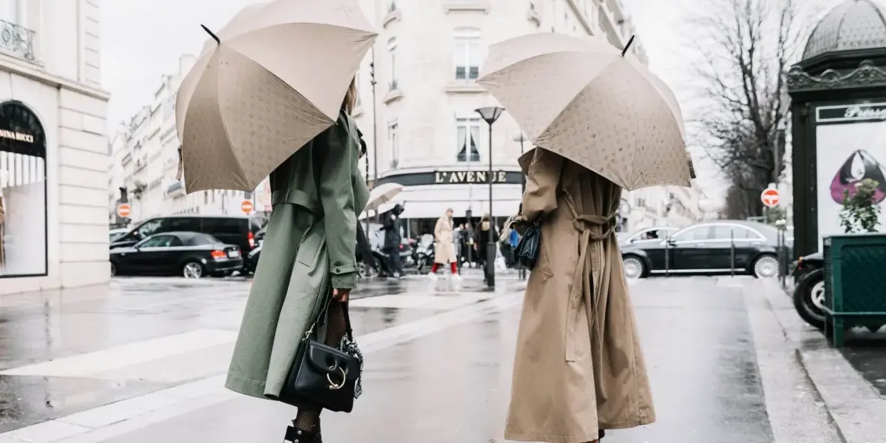 Dos mujeres con paraguas lucen elegantes gabardinas, como se llaman las chaquetas largas, en un día lluvioso en París.