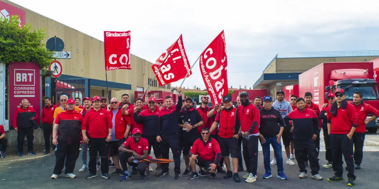 Un gruppo di lavoratori BRT, con bandiere rosse, manifesta per migliorare le condizioni di lavoro. Le loro opinioni su lavorare in Bartolini sono chiare.