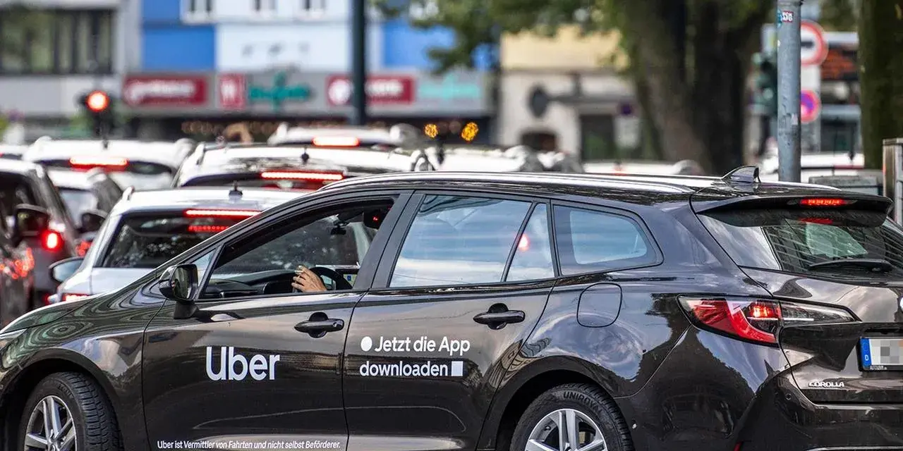 Ein dunkler Uber-Kombi steht im Stau. Die Aufforderung "Jetzt die App downloaden" ist gut sichtbar.