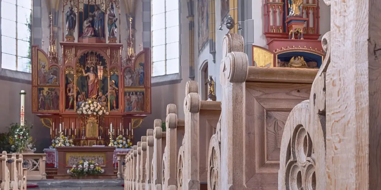 Drewniane ławki w kościele św. Jana w Warszawie, prowadzące do ołtarza z bogatymi zdobieniami i figurami.