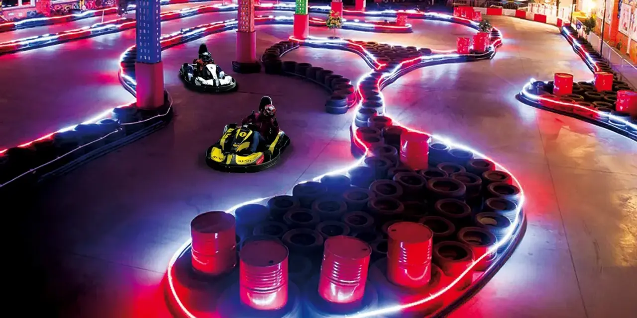 Tor kartingowy w stylu Canpol Wonderland, oświetlony neonami, z gokartami w akcji.