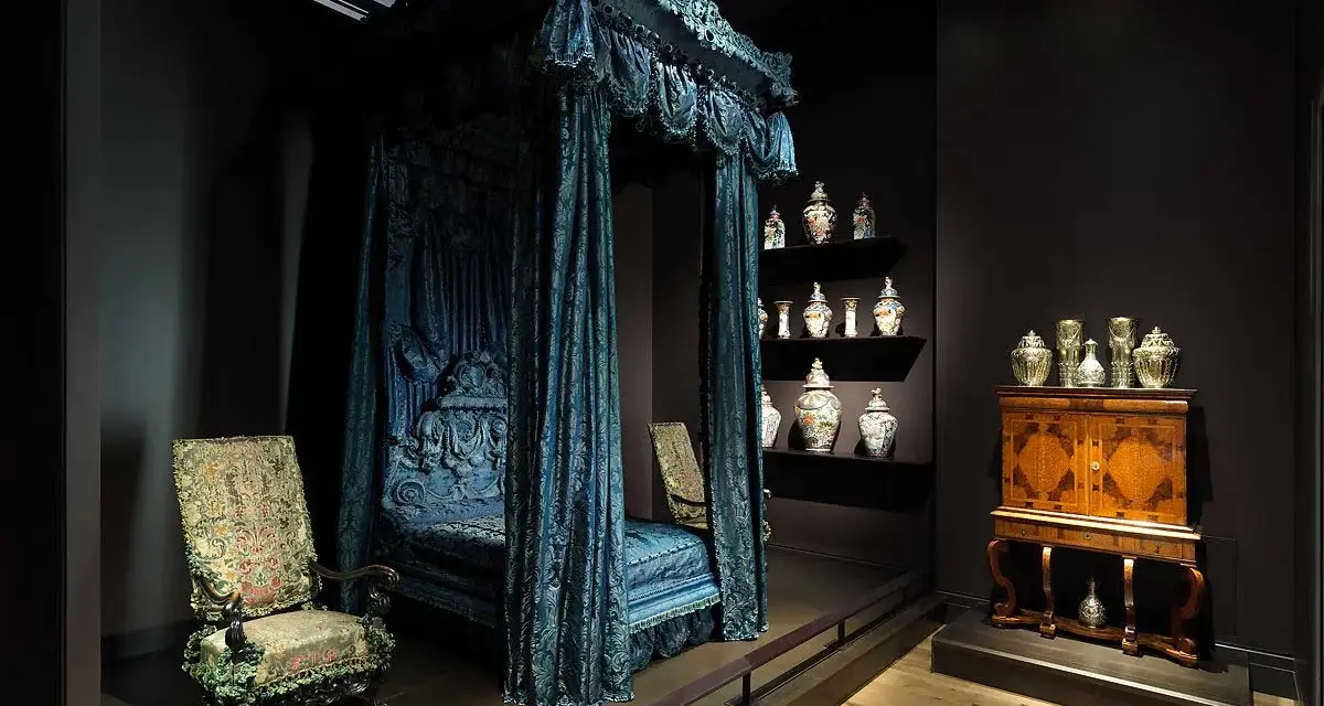 Cama con dosel azul, sillas ornamentadas y vitrinas con cerámica, como si fueran escenarios de cursos de arte online.