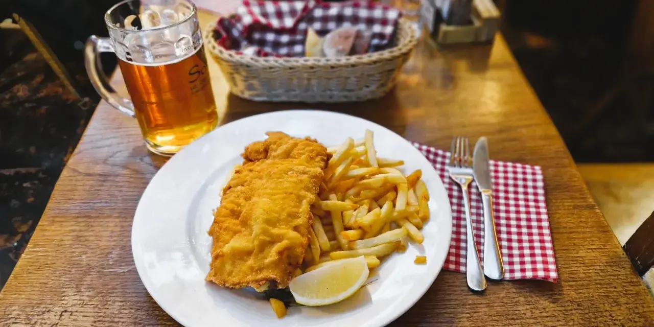 Piatto di pesce fritto e patatine fritte, con una birra chiara, un classico per scoprire cosa mangiare a Lubiana.