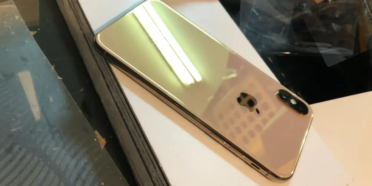 Błyszczący, złoty iPhone X leży na białej powierzchni.