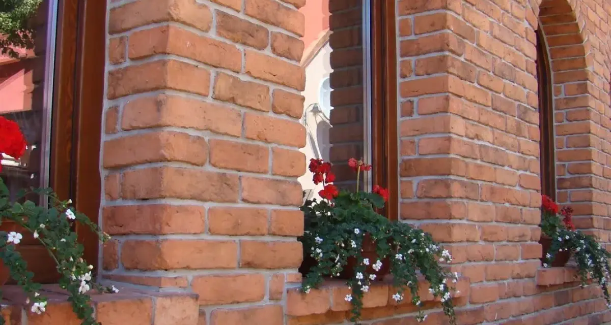 Elegancka elewacja z cegły klinkierowej, z kwitnącymi pelargoniami przy oknach. Sprawdź, jaka jest cegła klinkierowa cena!