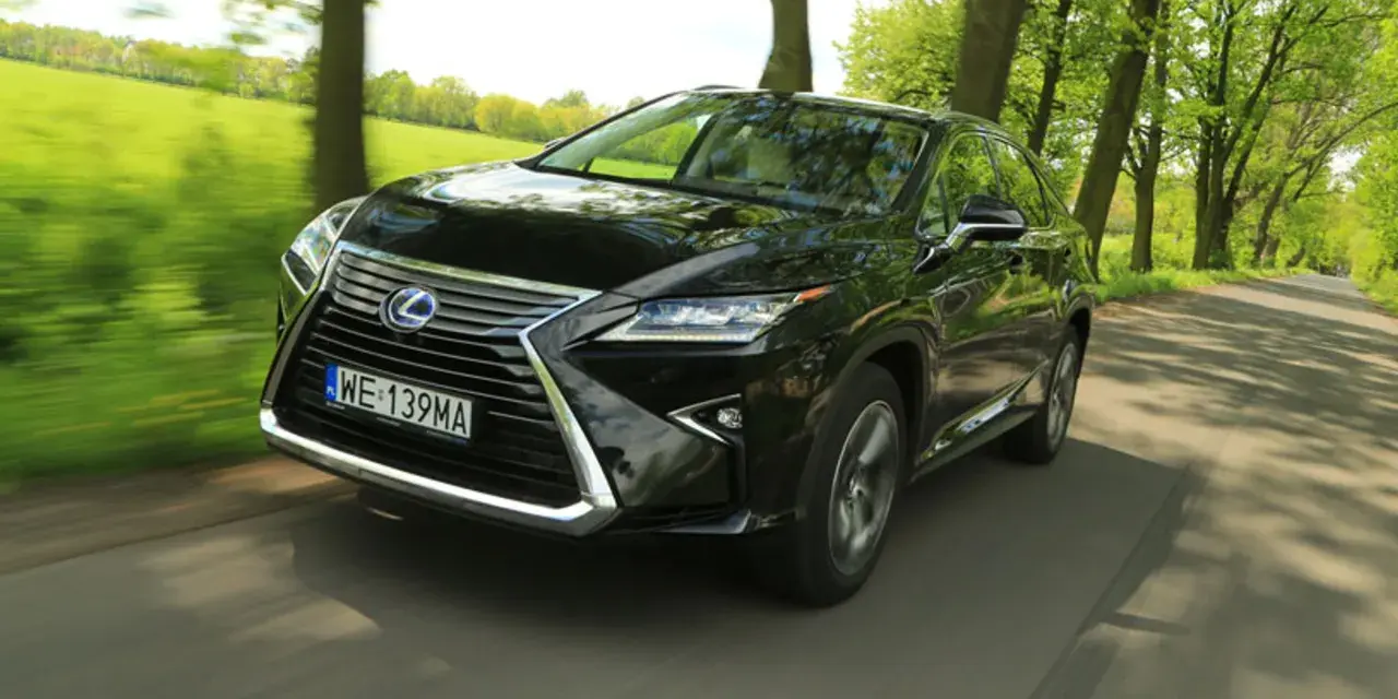 Czarny Lexus RX 450h pędzi po wiejskiej drodze, otoczony zielenią drzew i pól.