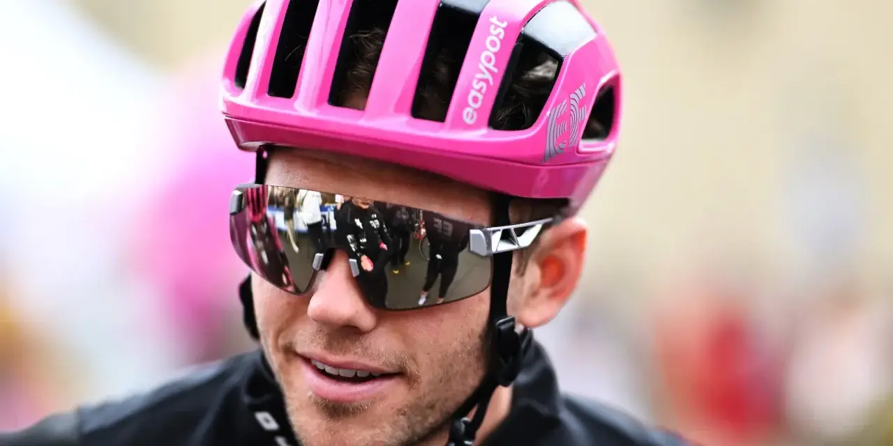 Cyclist Luke Lamperti smiles, wearing a bright pink helmet and reflective sunglasses.