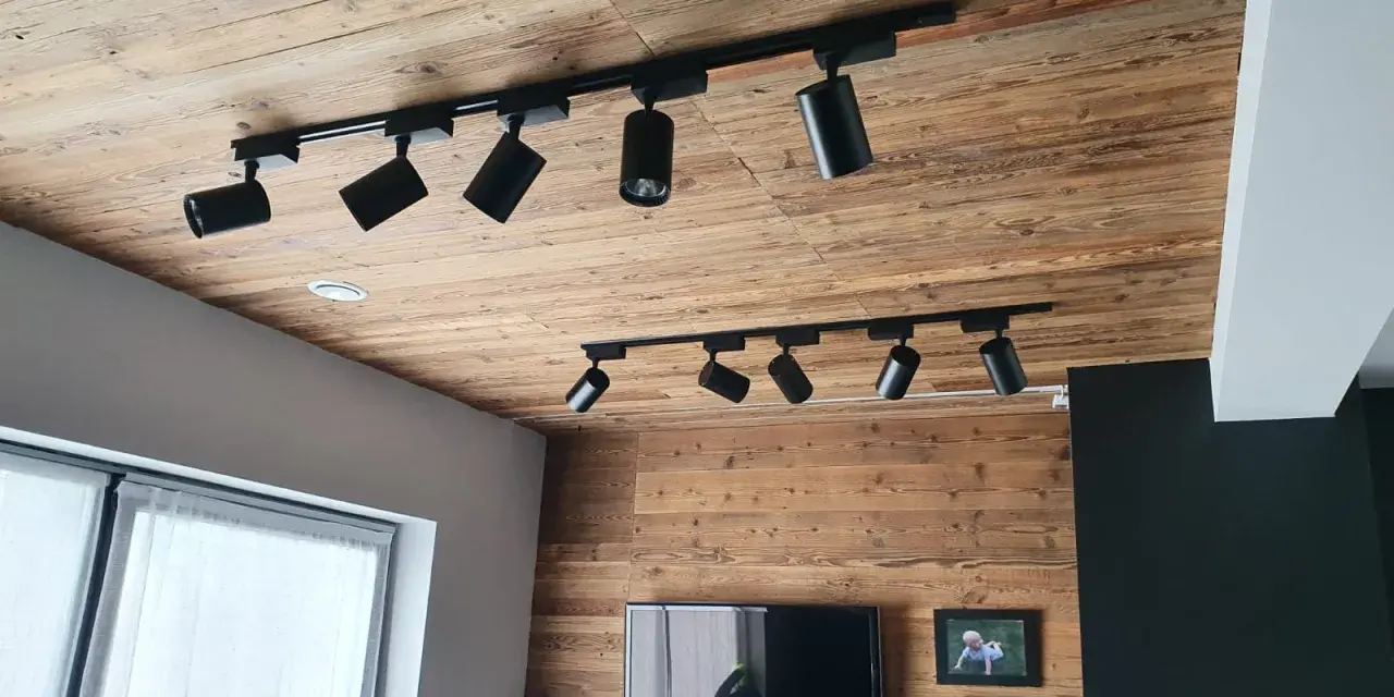 Nowoczesne reflektory na szynach, idealne jako oświetlenie, które przykleić na sufit. Drewniany sufit i ściana tworzą przytulną atmosferę.