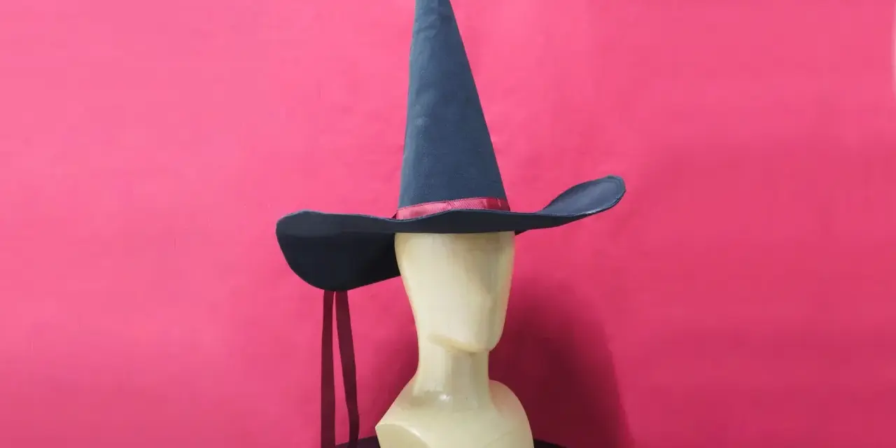 Un mannequin porte un patron chapeau pointu bleu foncé avec un ruban rouge. Deux rubans rouges pendent de chaque côté.