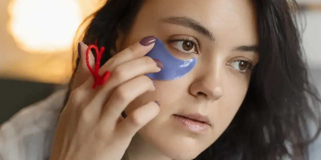 Una mujer se aplica parches de ojos morados. Muestra cómo se ponen los parches de ojos para un cuidado facial.