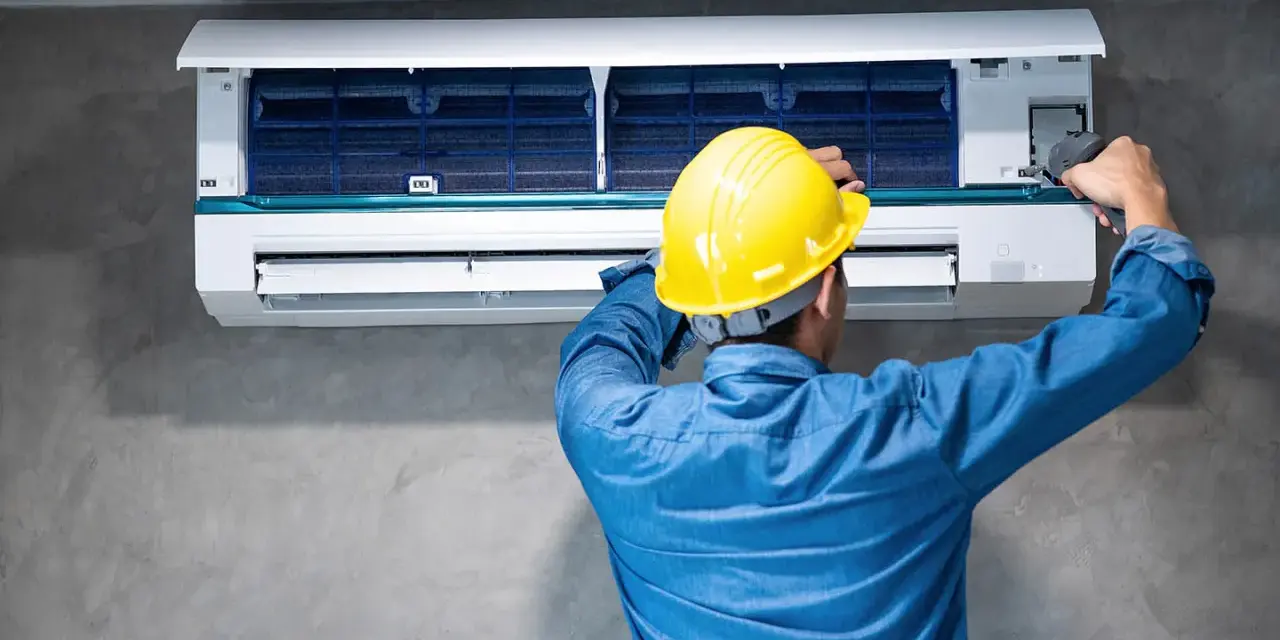 Técnico con casco amarillo revisa la unidad interior de aire acondicionado, buscando la causa del ruido.