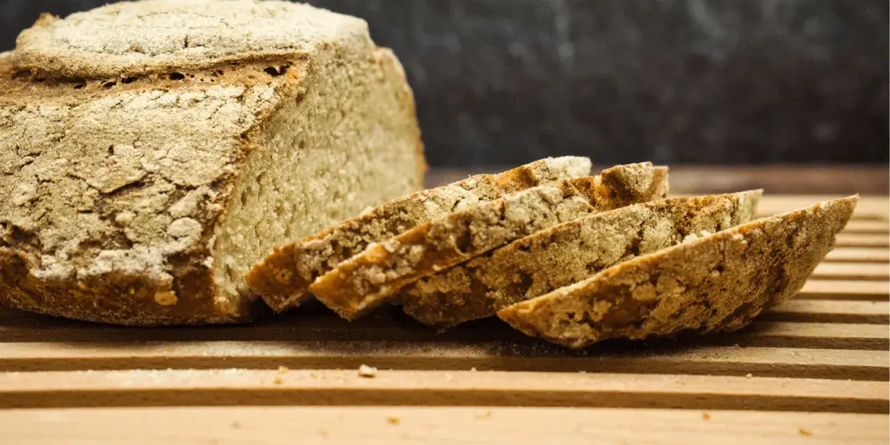 Ein rustikales, selbstgebackenes Brot liegt angeschnitten auf einem Holzbrett. Die Kruste ist knusprig, die Scheiben duften nach Tradition.