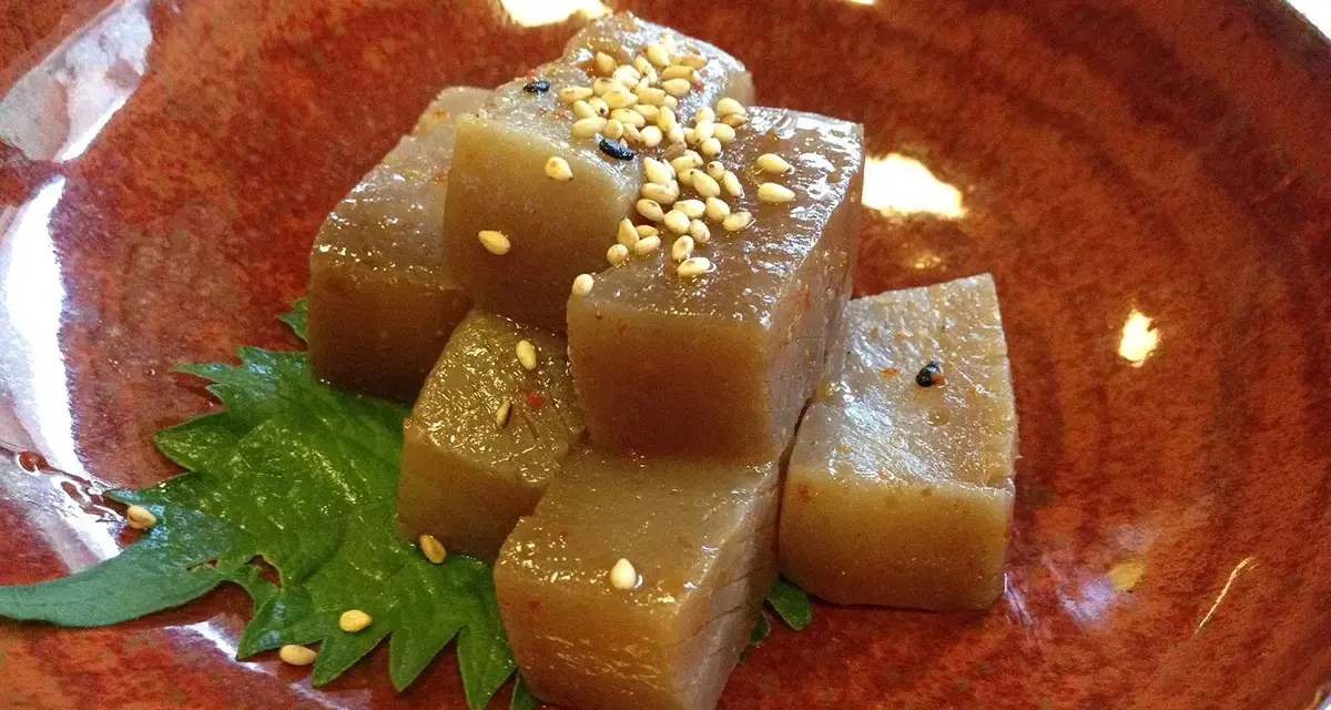 A simple dish of konjac jelly cubes, seasoned with sesame seeds and chili flakes, served on a green leaf in a rustic bowl. This is what monks eat.