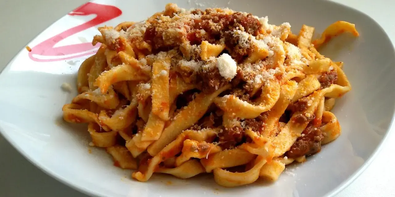 Un piatto invitante di tagliatelle al ragù, condite con abbondante parmigiano grattugiato.