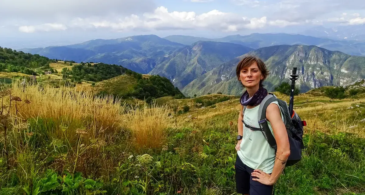 Donna con zaino e bastoncini da trekking ammira il panorama montuoso, un'emozione delle camminate FVG.