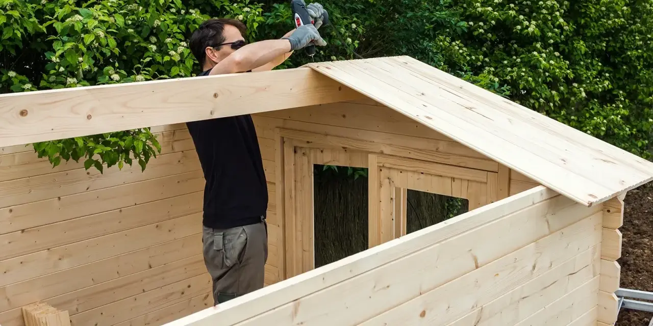 Hombre montando una caseta de madera. La madera clara y resistente es la mejor madera para exterior.