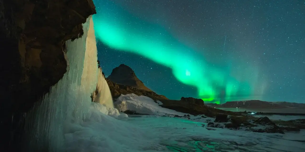 Lodowy wodospad i zorza polarna na nocnym niebie. Islandia w styczniu, magiczny widok.
