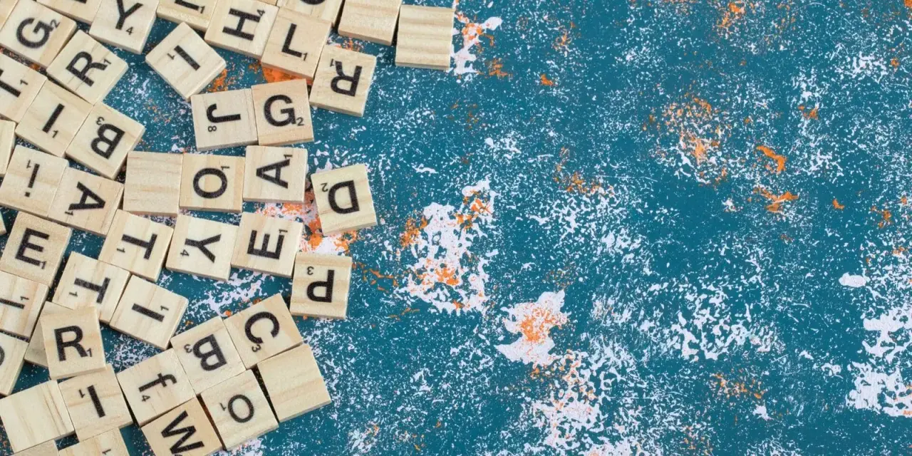 Fichas de letras de madera esparcidas, algunas formando palabras con w, sobre un fondo azul texturizado con salpicaduras blancas y naranjas.