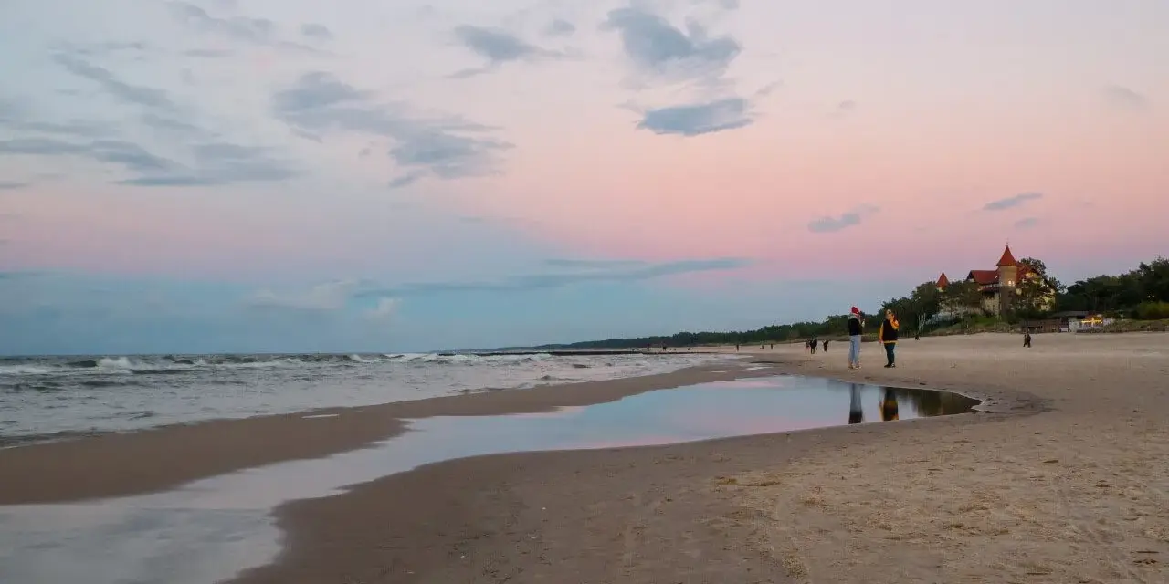 Zachód słońca nad morzem w kurorcie niedaleko Lęborka. Piękne, pastelowe niebo odbija się w wodzie na plaży.