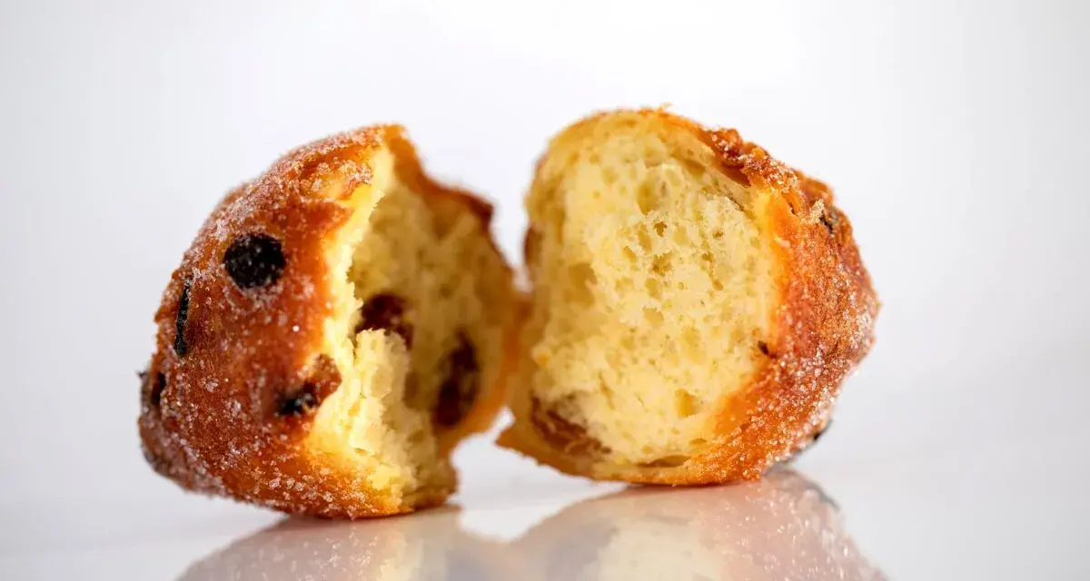 Frittelle veneziane, dolci e soffici, con uvetta e zucchero, spezzate a metà per mostrare l'interno invitante.