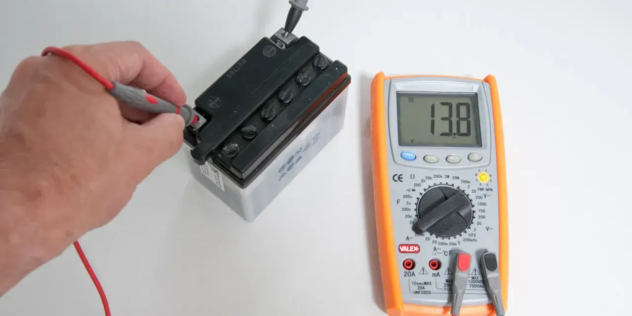 Una mano usa il multimetro per misurare la tensione di una batteria, mostrando 13.8V.