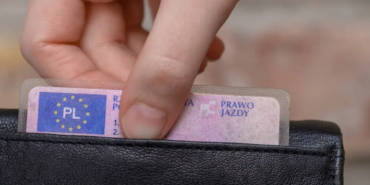 Dłoń wkłada do czarnego portfela polskie prawo jazdy. Widoczny numer blankietu prawa jazdy.