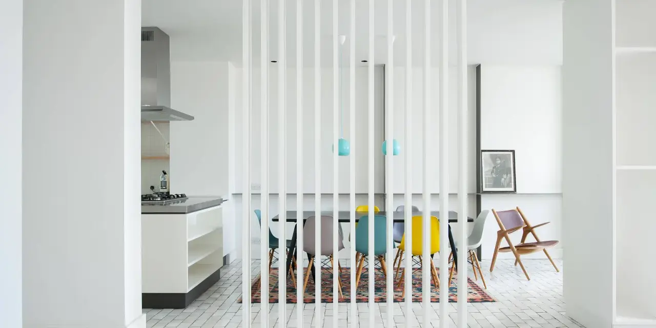 Elegante solución para dividir salón en dos ambientes. Cocina moderna y comedor con sillas de colores, separados por una celosía blanca.