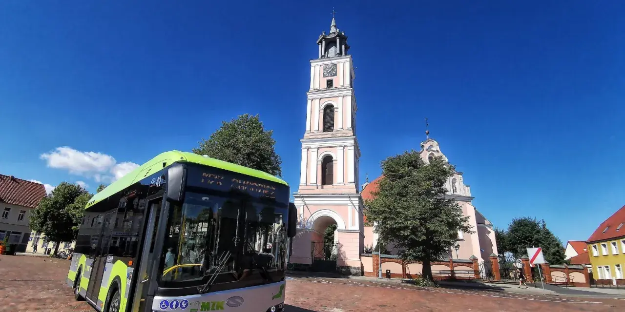 Zielony autobus MZK Chodzież czeka na pasażerów pod wieżą kościoła. Sprawdź mzk chodzież rozkład jazdy i zaplanuj podróż!