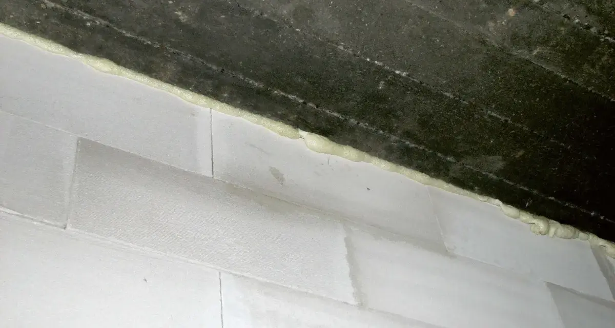 Piana montażowa wypełnia szczelinę między betonowym stropem a białą ścianą z bloczków, tworząc dylatację.