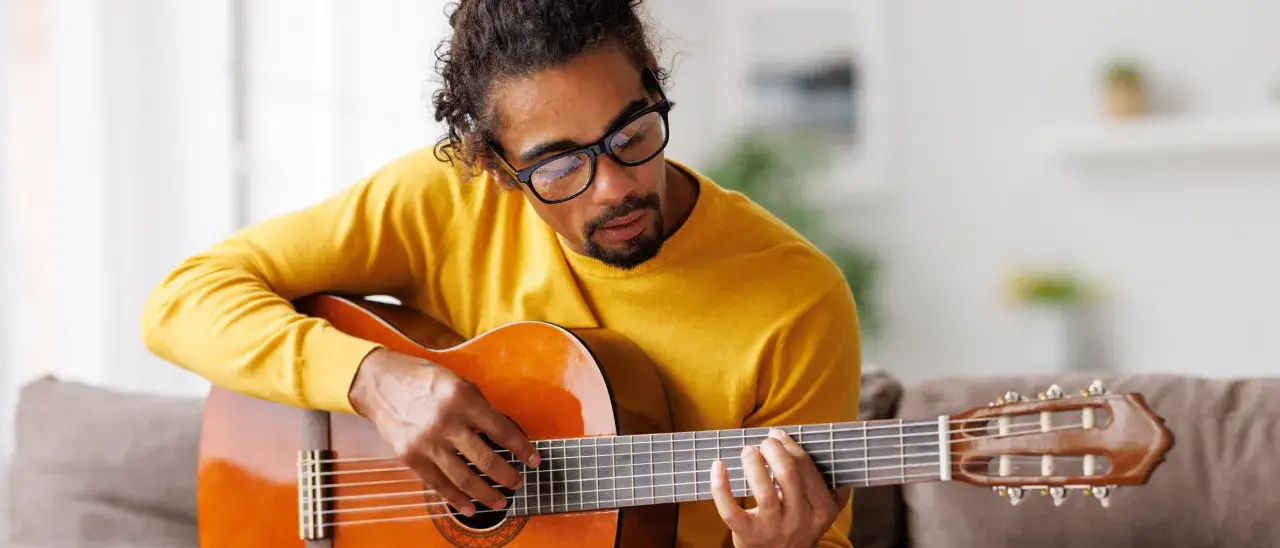 Mann mit Brille hält eine Gitarre und spielt darauf.