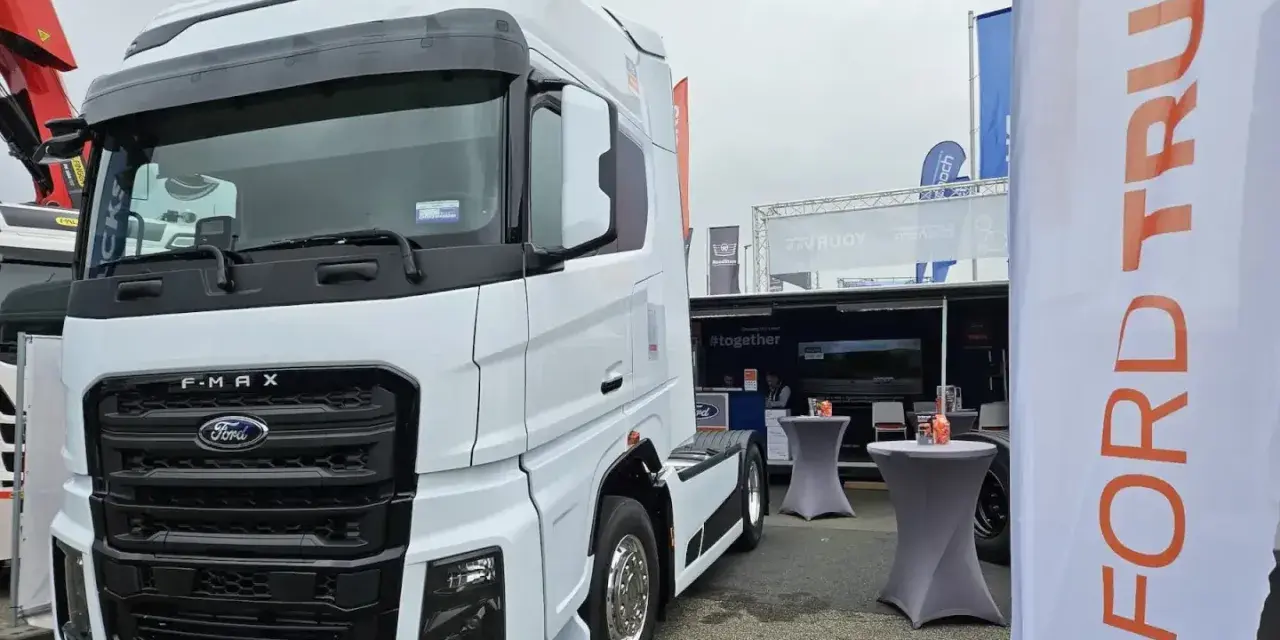 Biały Ford F-MAX prezentuje się na wystawie, obok banerów z logo Ford Trucks.