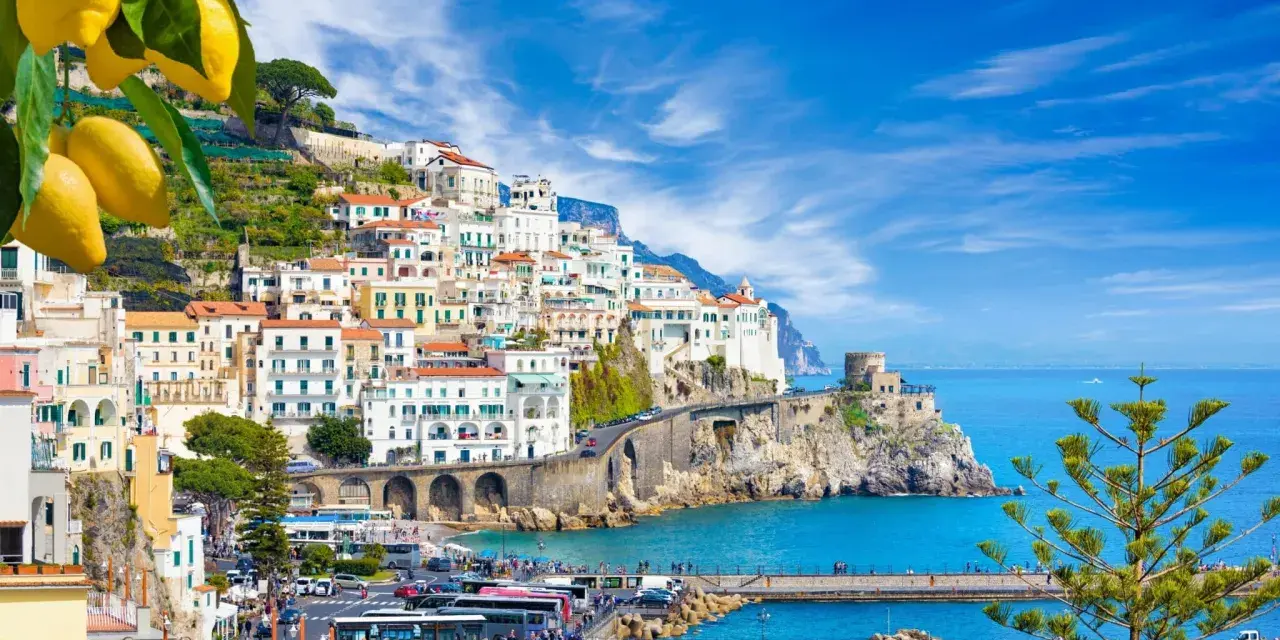 Costiera Amalfitana, un sogno di **Italia in moto** tra limoni e mare blu. Case bianche aggrappate alla roccia, un borgo pittoresco.