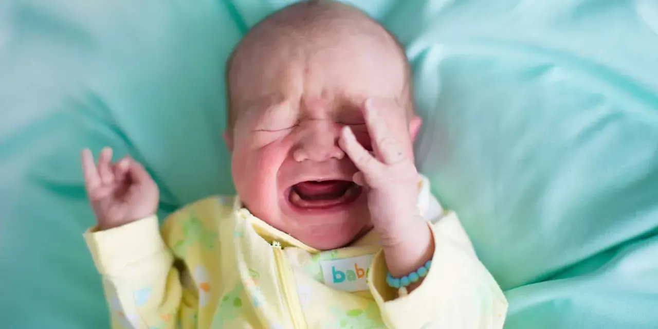 Ein **baby weinen** auf einem türkisfarbenen Tuch, mit geschlossenen Augen und einer Hand vor dem Gesicht.