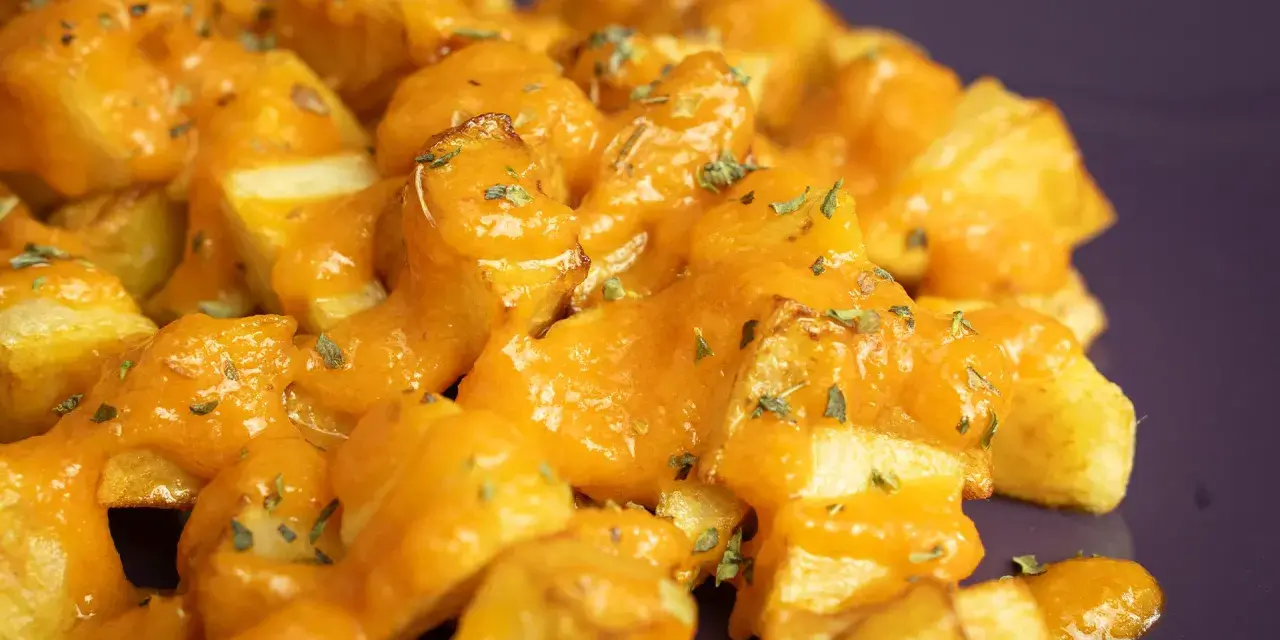 Patatas bravas crujientes cubiertas con una salsa naranja cremosa y hierbas picadas.