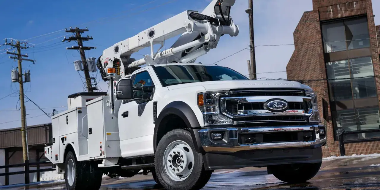 Biały Ford F650 z podnośnikiem koszowym gotowy do pracy przy liniach energetycznych.