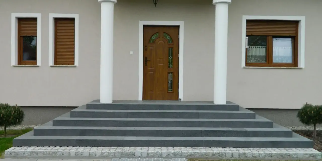 Elegancka, zewnętrzna klatka schodowa w domu jednorodzinnym prowadzi do brązowych drzwi z witrażem.