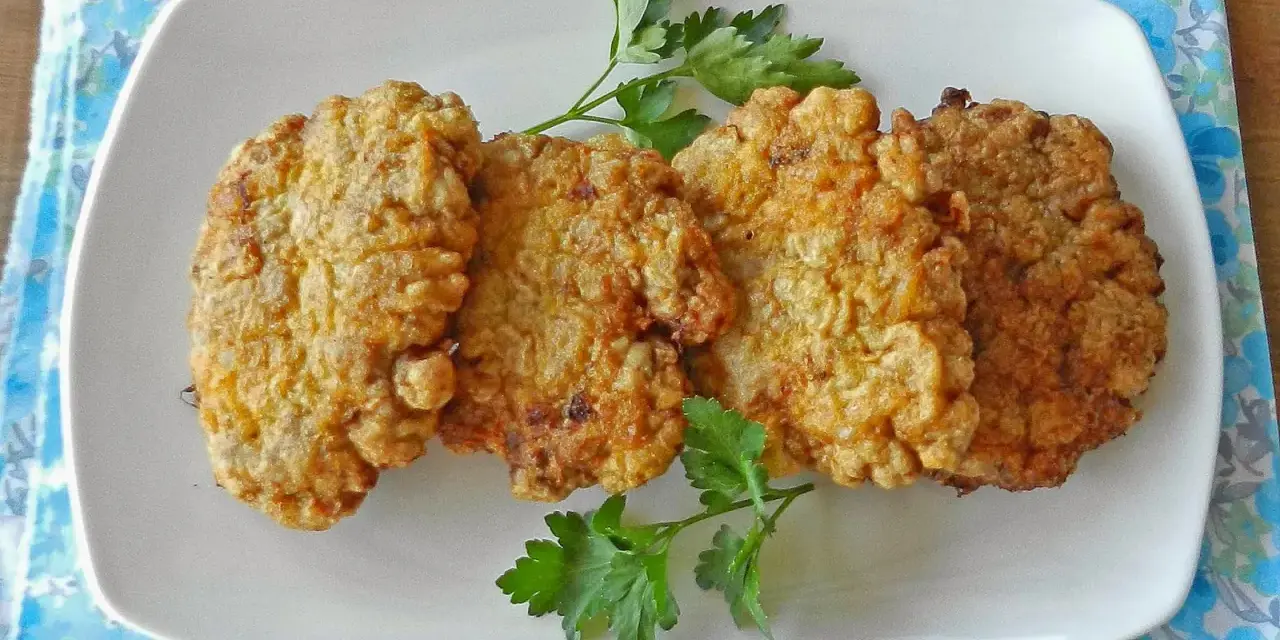 Cuatro filetes rusos dorados y crujientes servidos en un plato blanco con perejil.