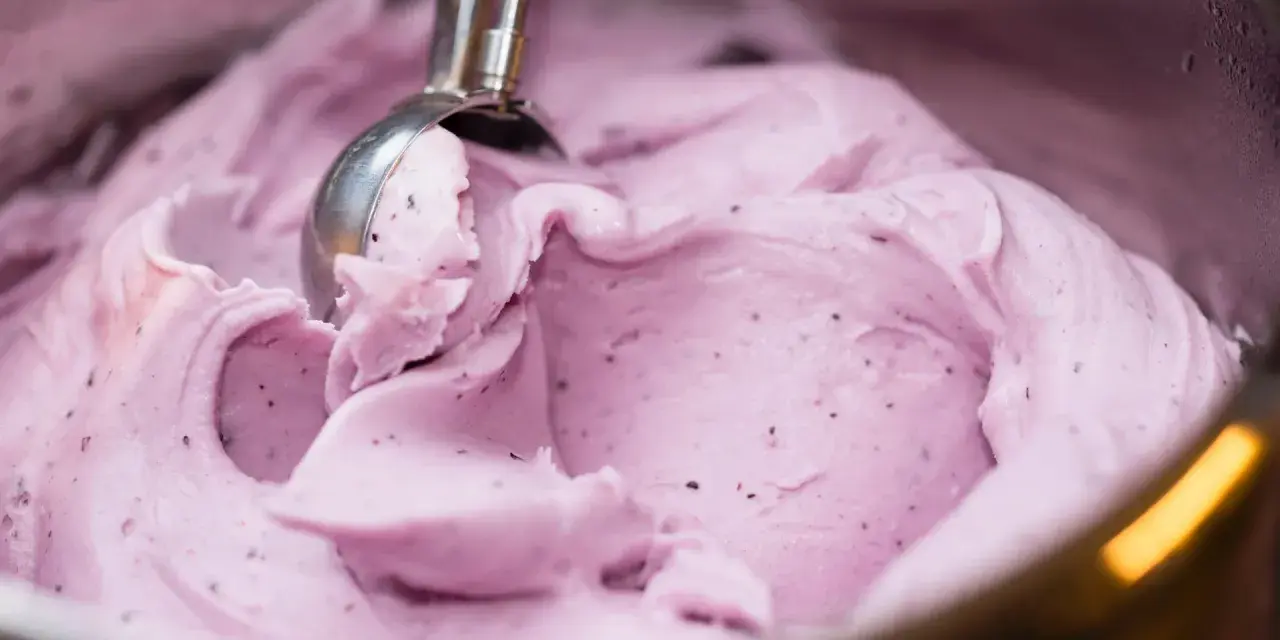 Ein Löffel nimmt eine Portion cremiges, kalorienarmes Eis mit Beerenstücken auf.