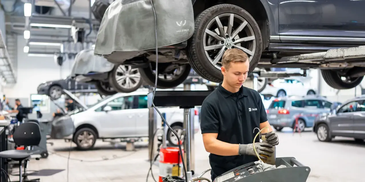 Mekaniker arbetar med en bil på en verkstad. Frågan "hur lång tid tar en bilservice" kan variera beroende på vad som behöver göras.