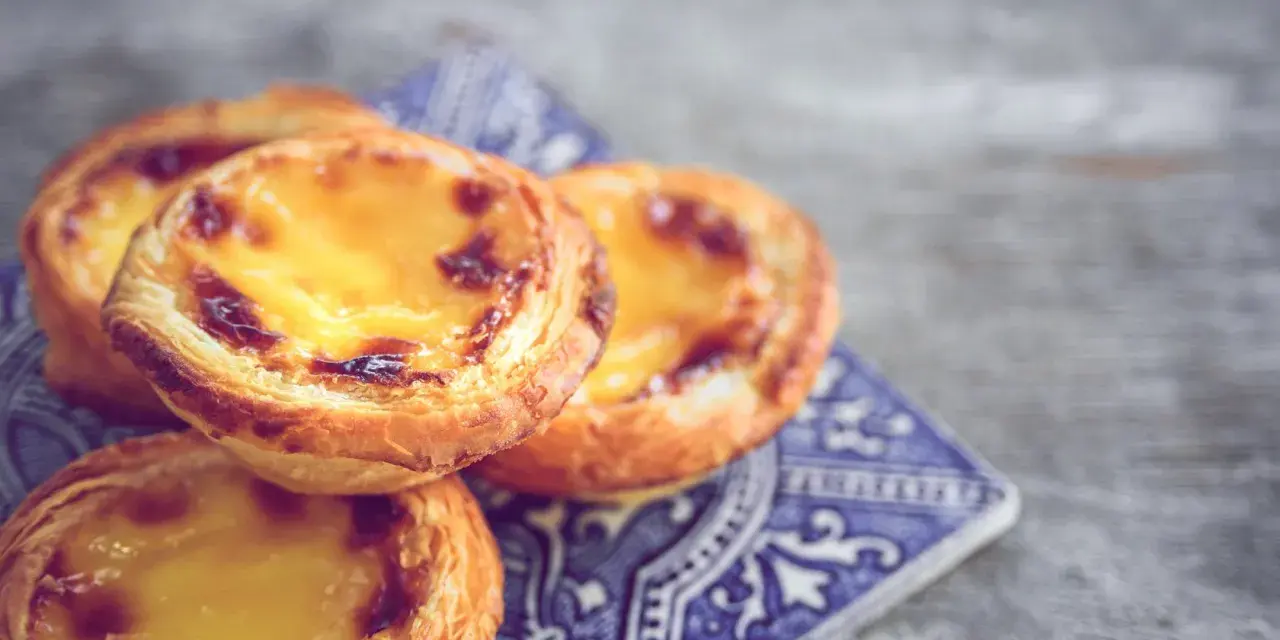 Ein Stapel goldbrauner, karamellisierter Pastel de Nata auf einer blauen Kachel.