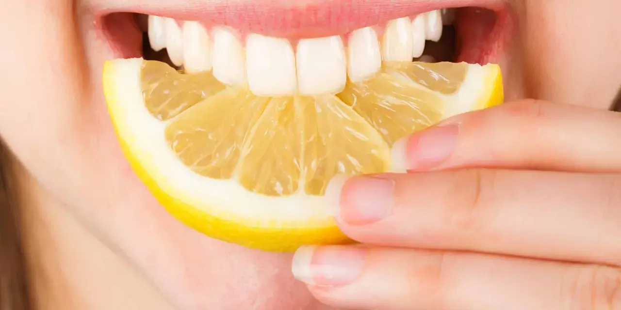 Une personne tient une tranche de citron près de sa bouche ouverte, révélant des dents blanches. Le citron est connu pour ses bienfaits sur la peau.
