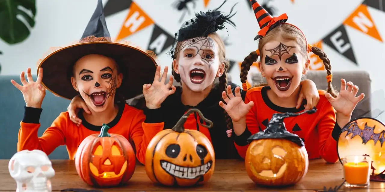 Tre barn med läskig ansiktsmålning och halloweenkostymer njuter av halloween aktiviteter med pumpor och dekorationer.