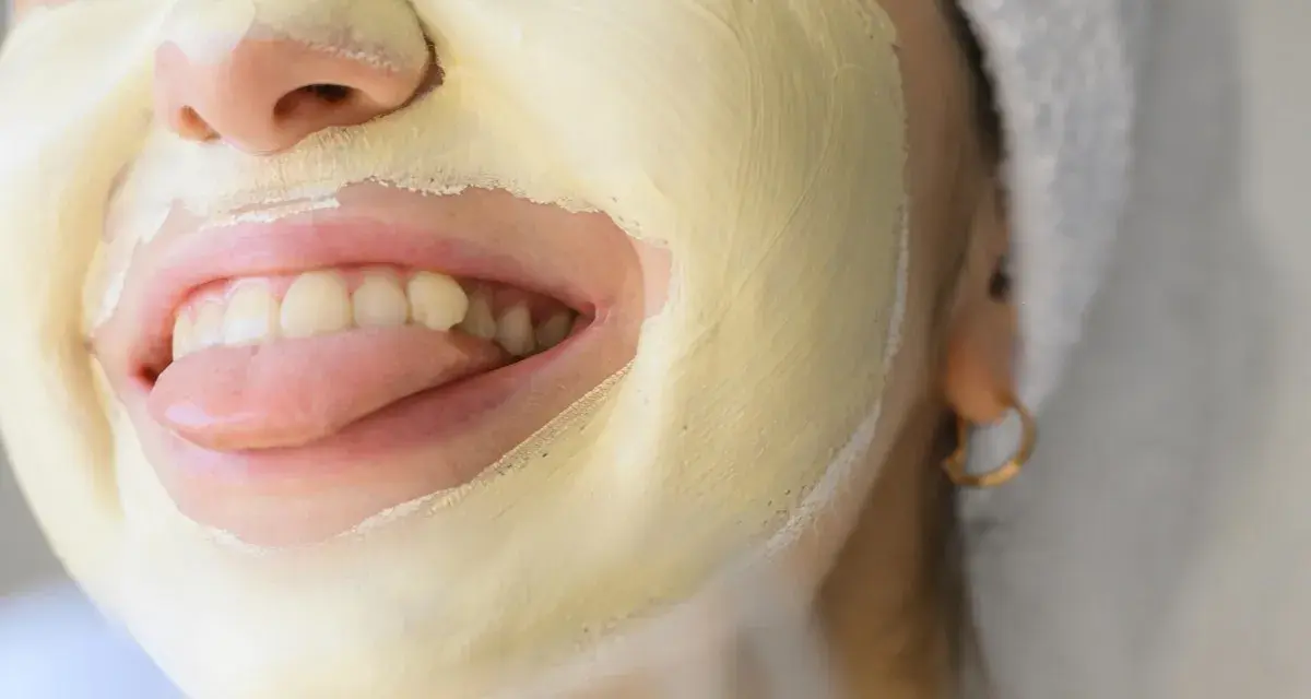 Una mujer se divierte con una mascarilla facial amarilla, sacando la lengua.