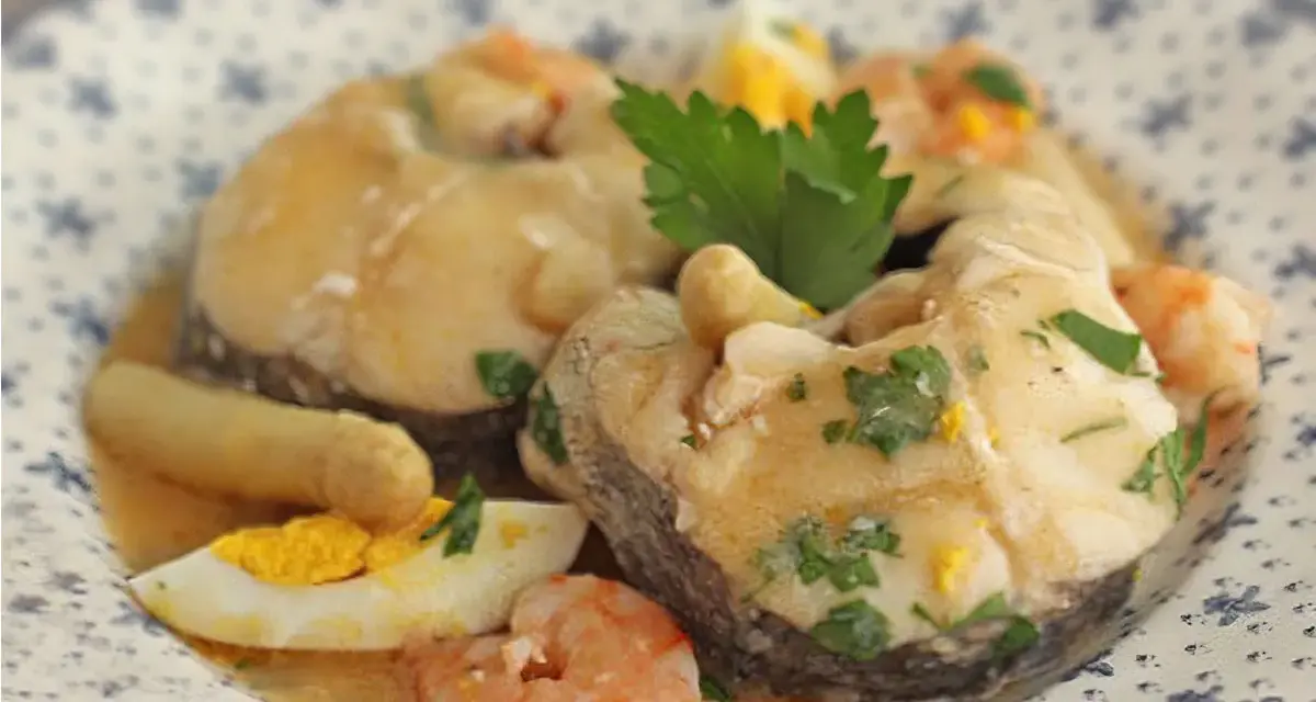 Merluza a la vasca con gambas, huevo duro y perejil, servida en un plato con diseño floral.